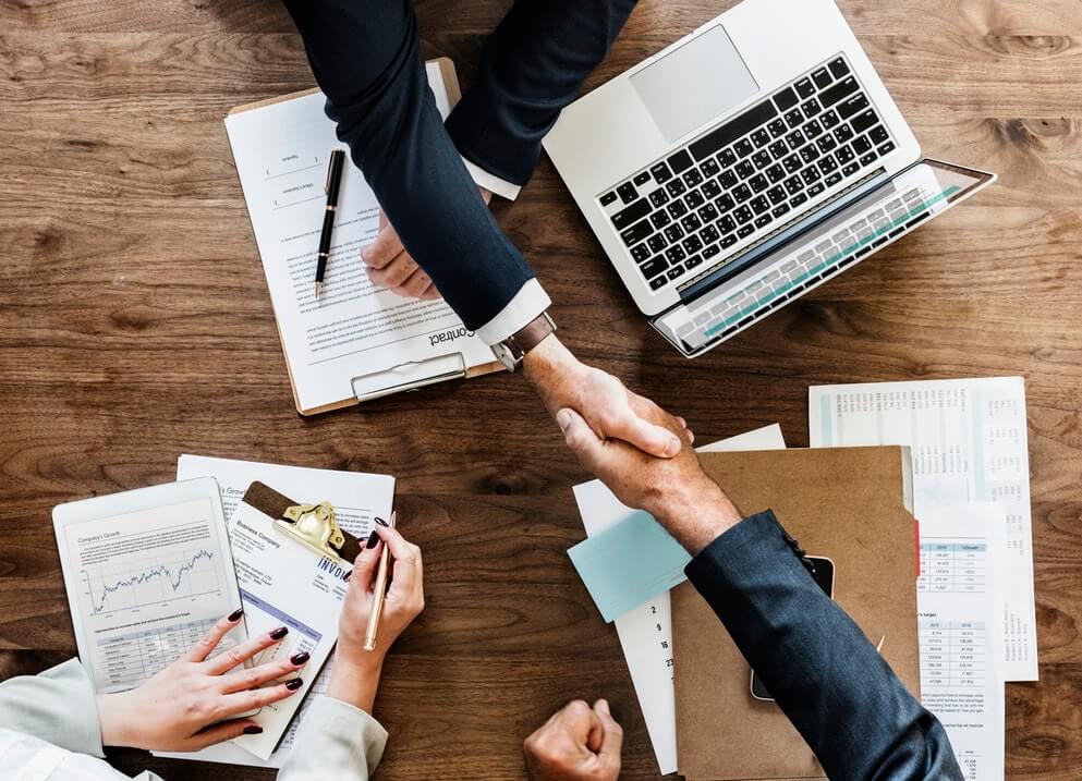 Two Business People hand shaking above work desk