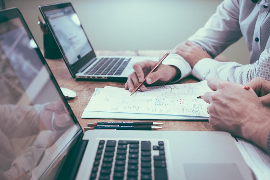 Sideview shot of two businessmen's hands on their laptops following the ebay inventory management tips to keep their customers content.