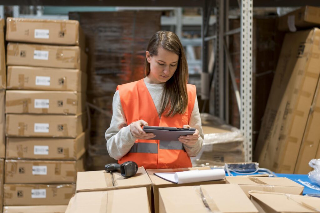 Image of a woman with tablet in a warehouse with barcode scanner and clipboard in front of her.