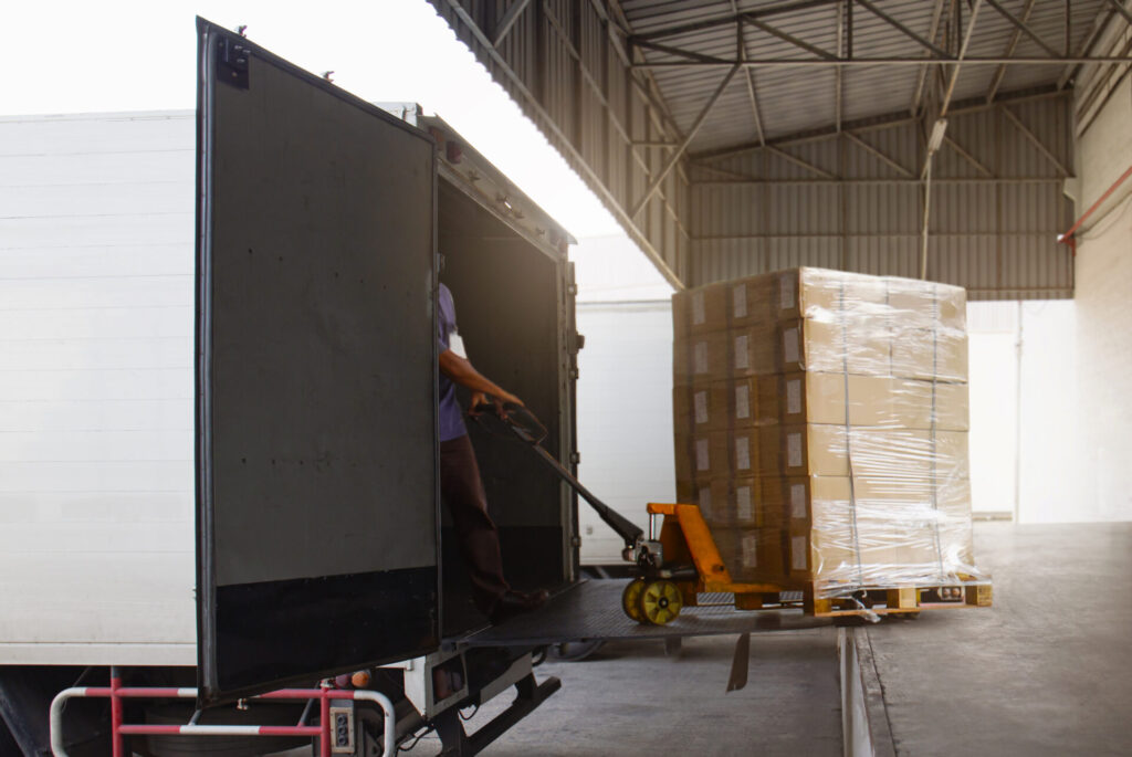 A person is unloading a transfer order from a white truck at a warehouse or fulfillment center.