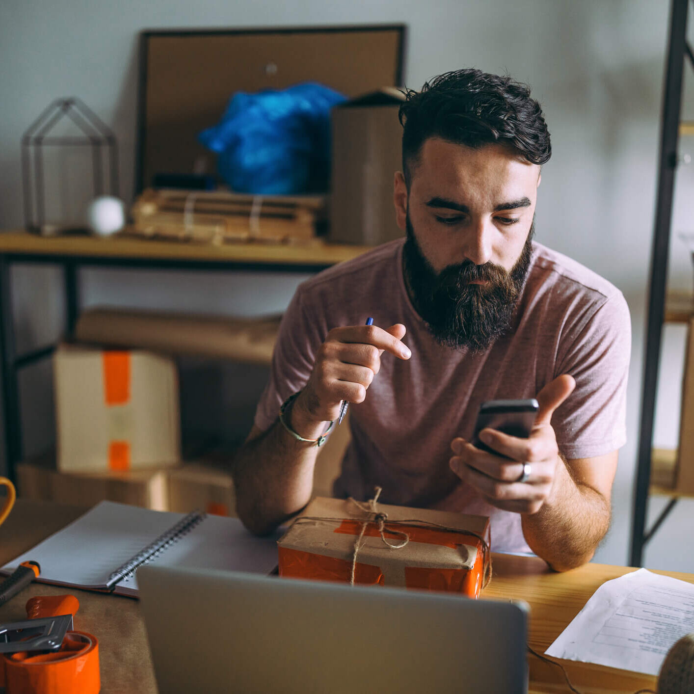 He using app for smart phone tracking delivery package small business owner with package in front of him looking at his phone